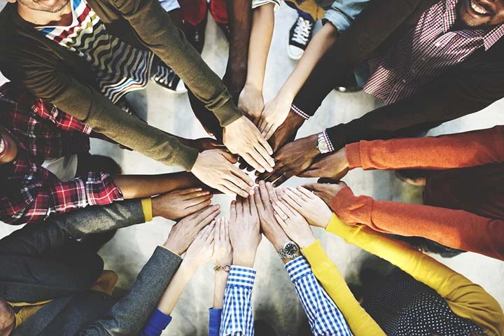 Un grupo de personas reúne sus manos en el centro de una mesa.