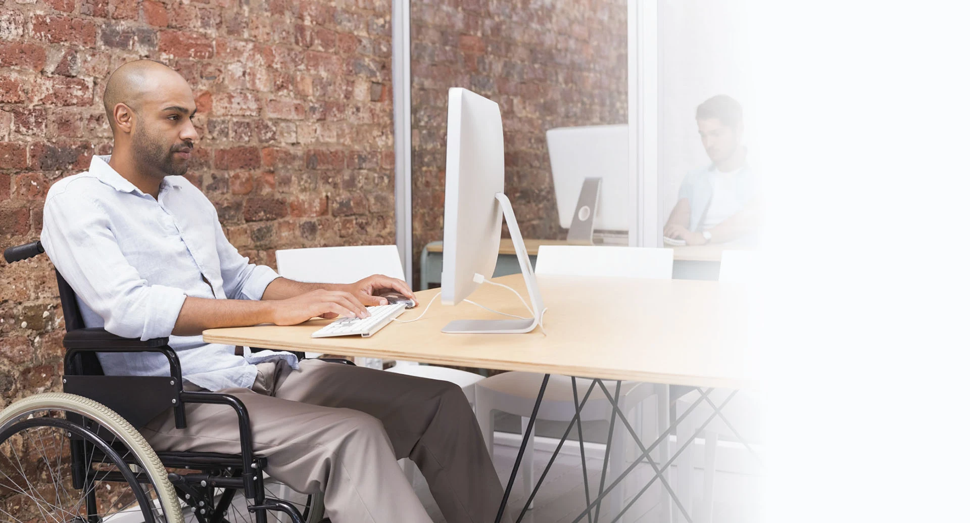 Un hombre en silla de ruedas trabaja frente a un computador en una oficina.